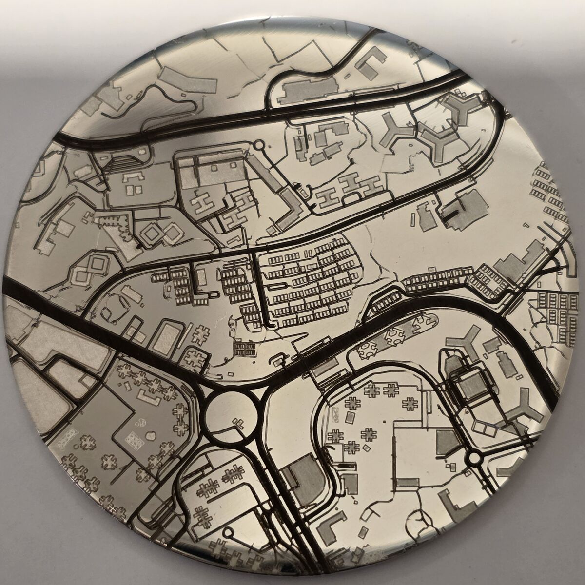 A polished engraved coin photographed from above, its whole face covered in a street map with roads, roundabouts, houses and trees